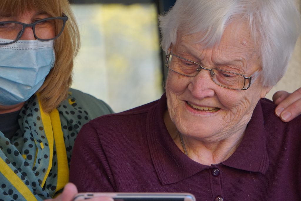 Woman with mask helping elder woman with videocall