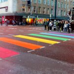 An urban commercial road where many people are waiting to walk on coloured crossing lines