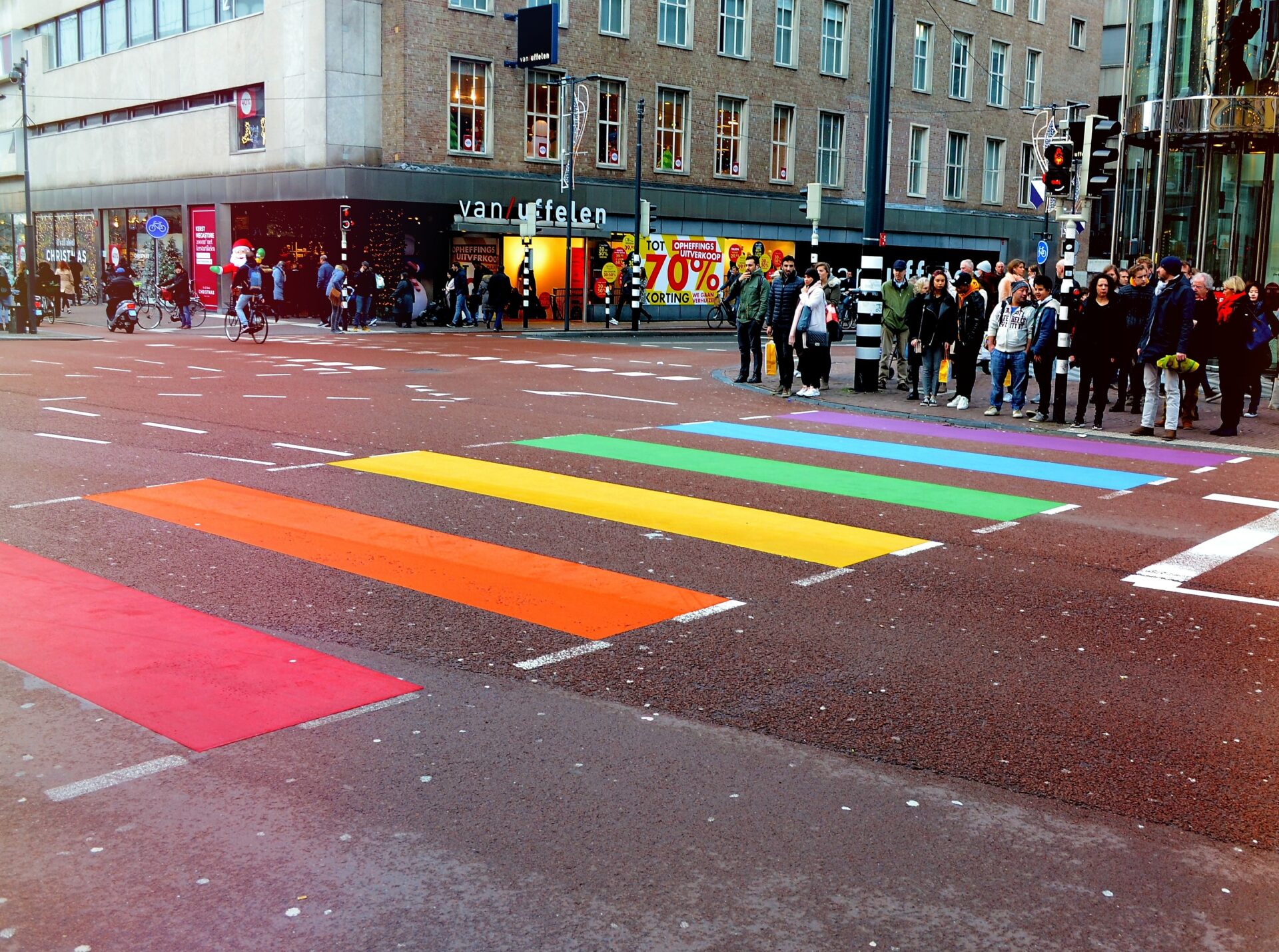 An urban commercial road where many people are waiting to walk on coloured crossing lines